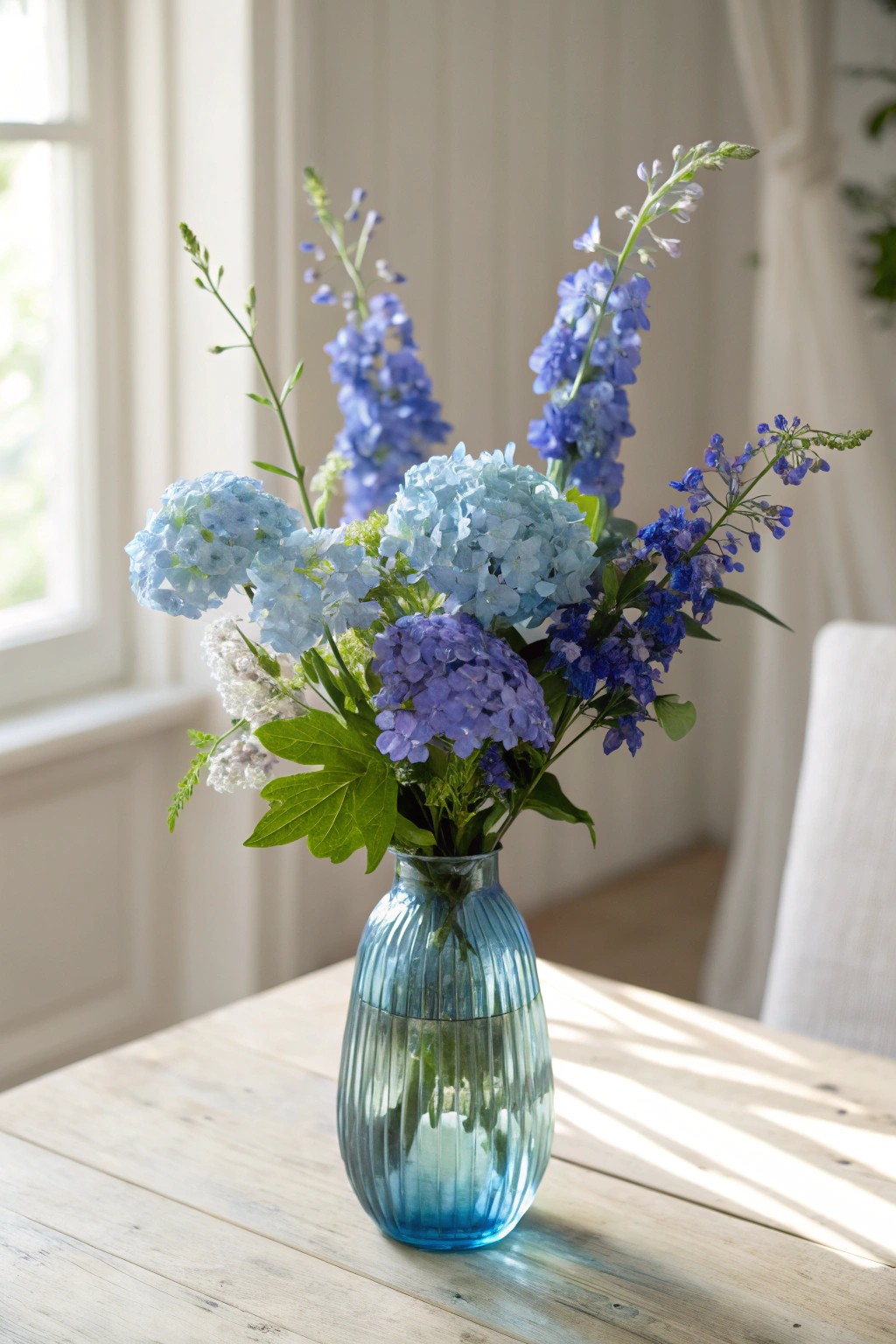 Bring natural vibrance home with a blue floral centerpiece in a handcrafted glass vase.