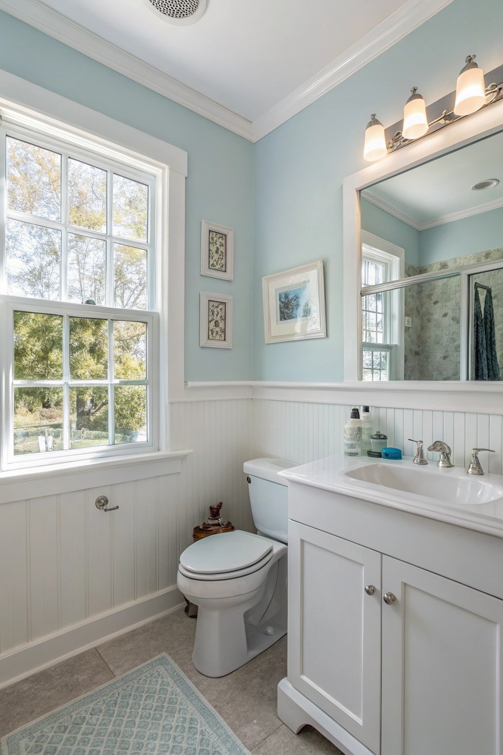 A small bathroom painted in a gentle blue, glowing with natural and artificial light.