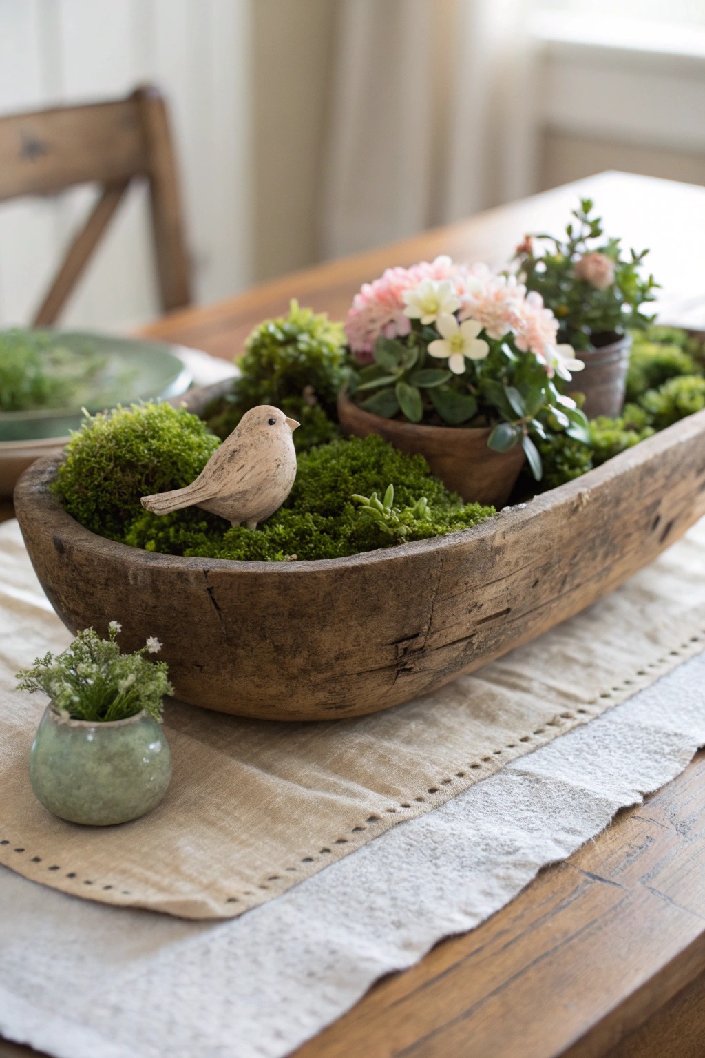 A vintage dough bowl brimming with springtime charm—moss, blooms, and a whimsical bird centerpiece.